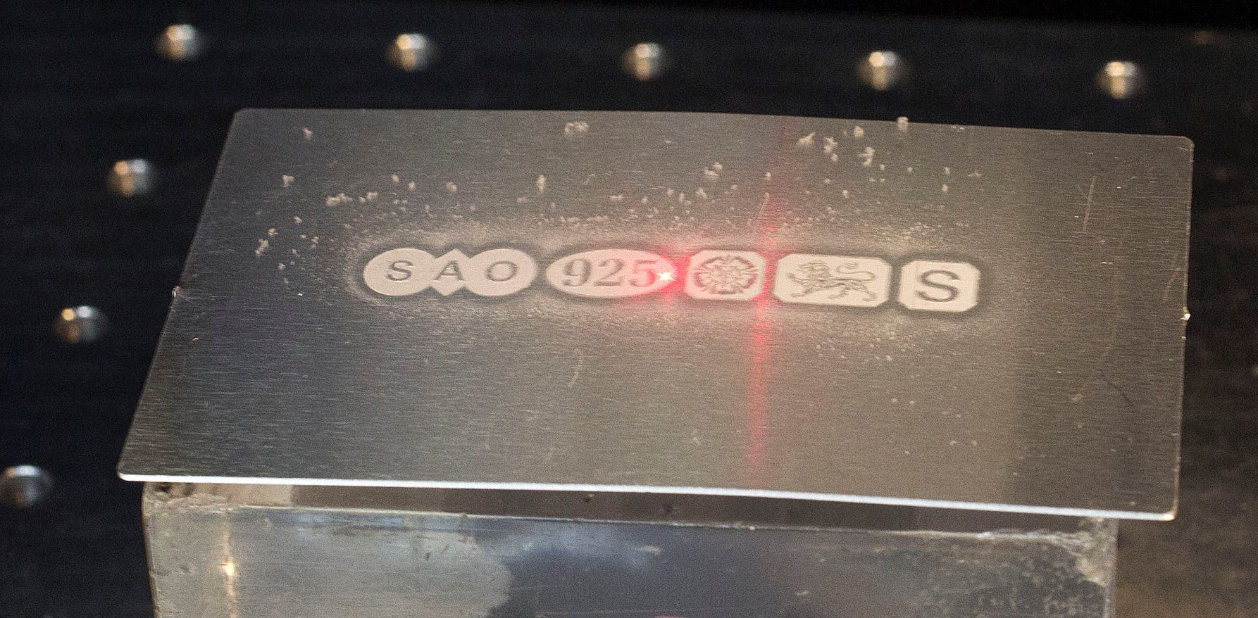 Metallic plaque with engraved text on a dark background. Shows laser hallmarking in action.