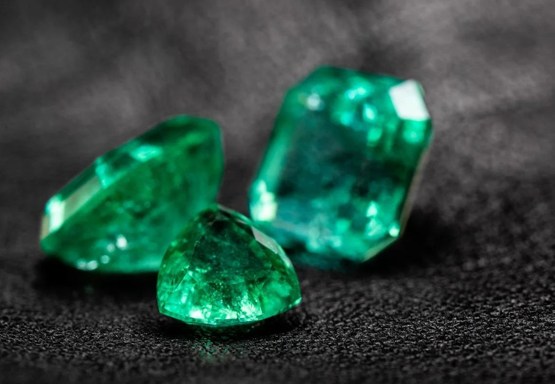 Three green emeralds on a dark textured surface