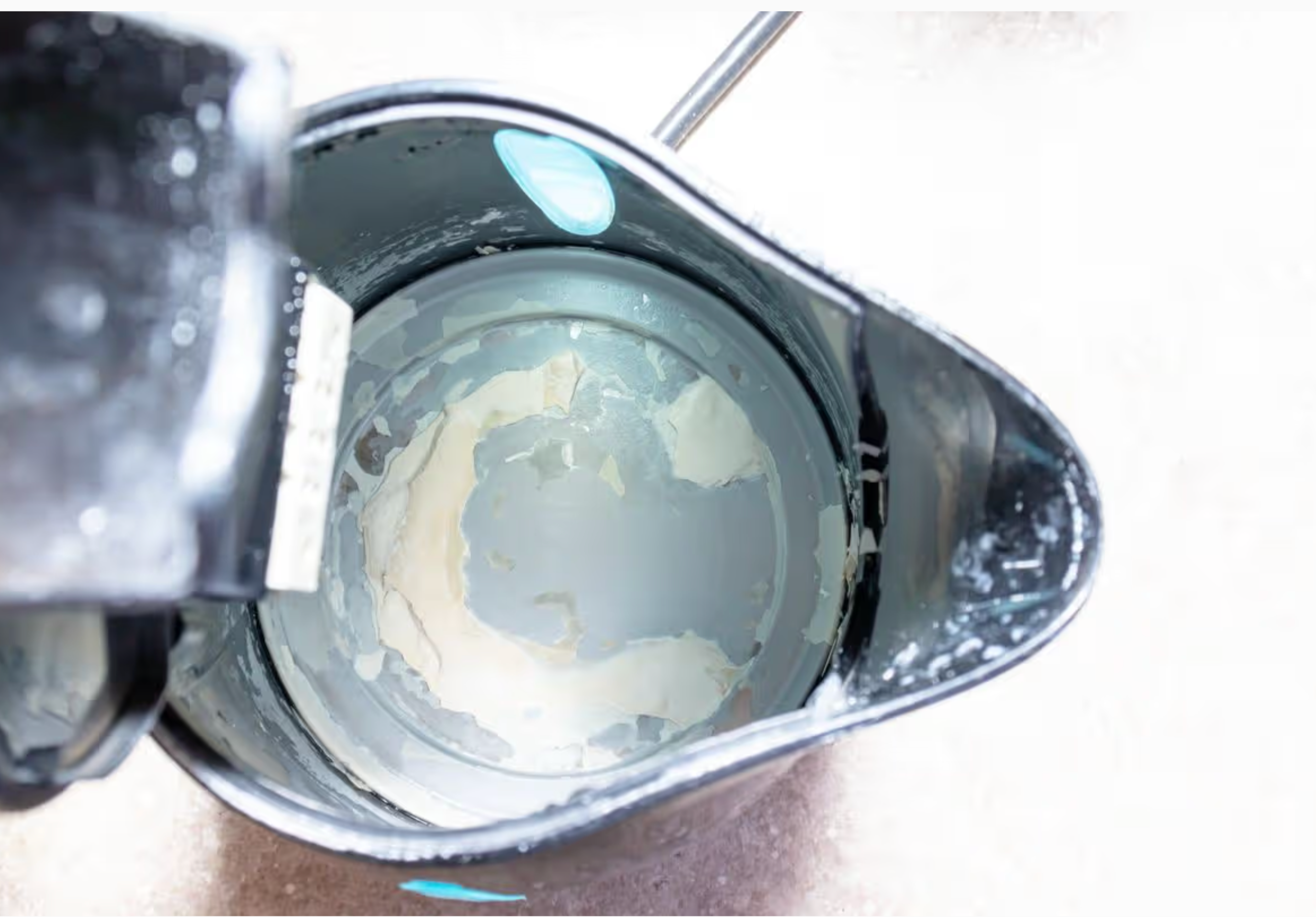 Close-up of a kettle with a white substance inside, on a light background. Inside the kettle is visible limescale.