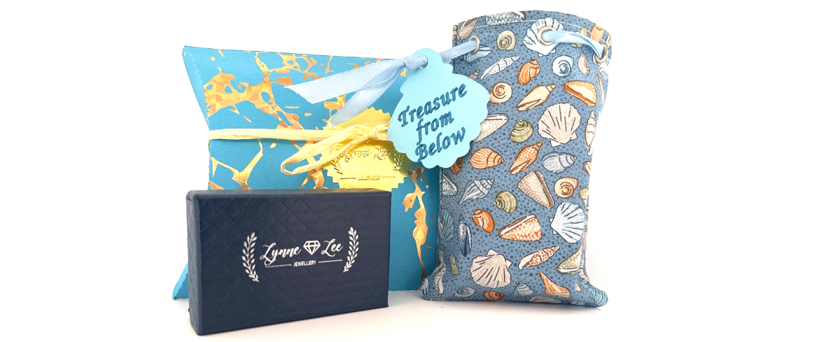 Gift set with a blue box, yellow ribbon, and a decorative bag with shell pattern on a white background.