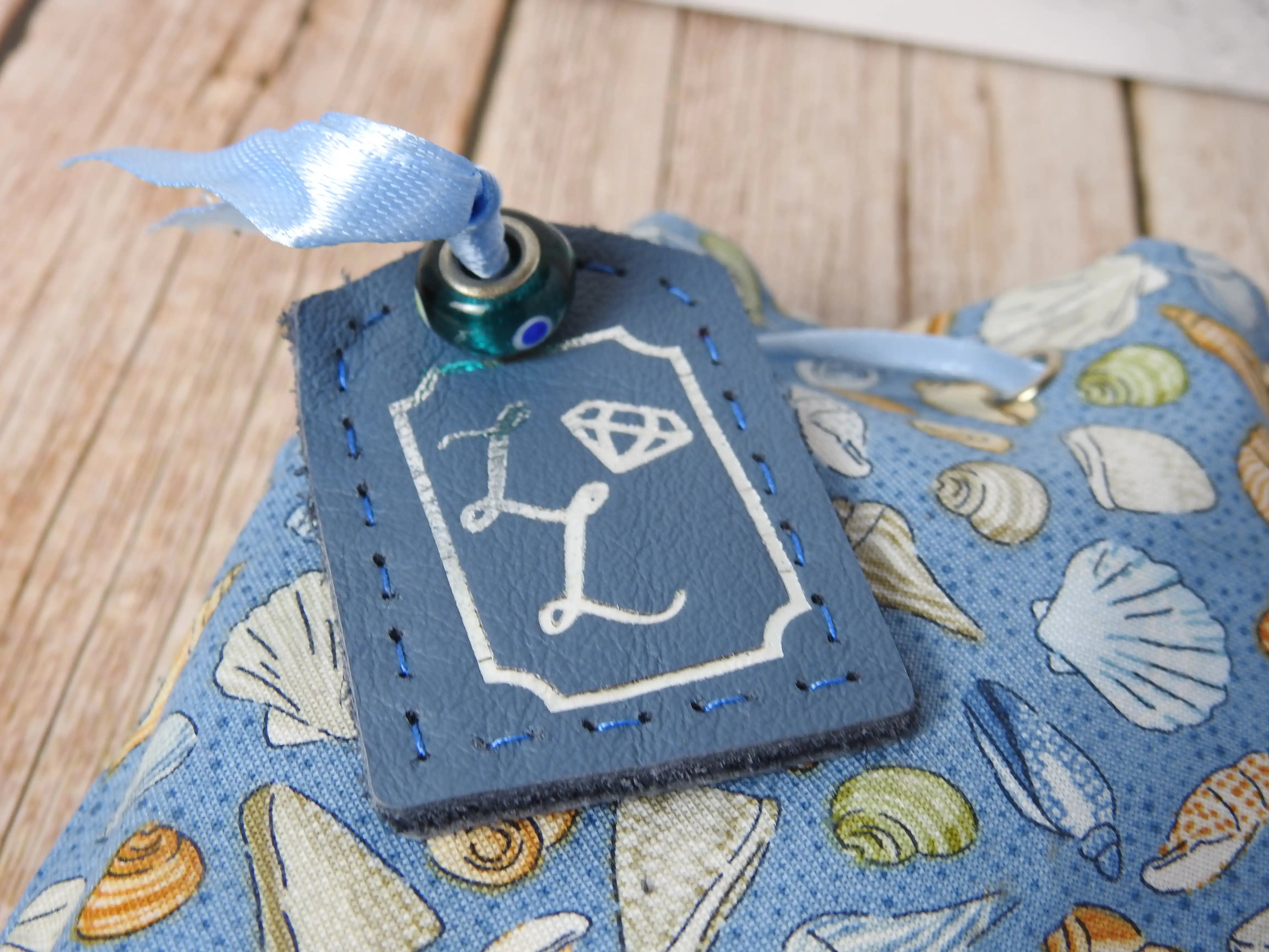 Blue leather tag, silver foil stamped, resting on top of themed bag, tied with ribbon and glass bead.