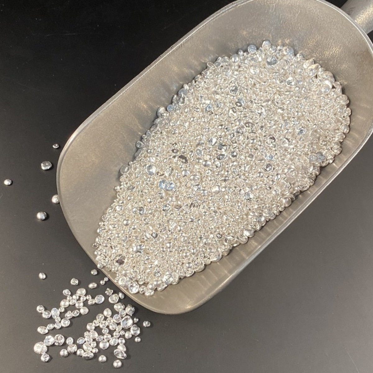 Metal scoop filled with small silver grain on a dark surface