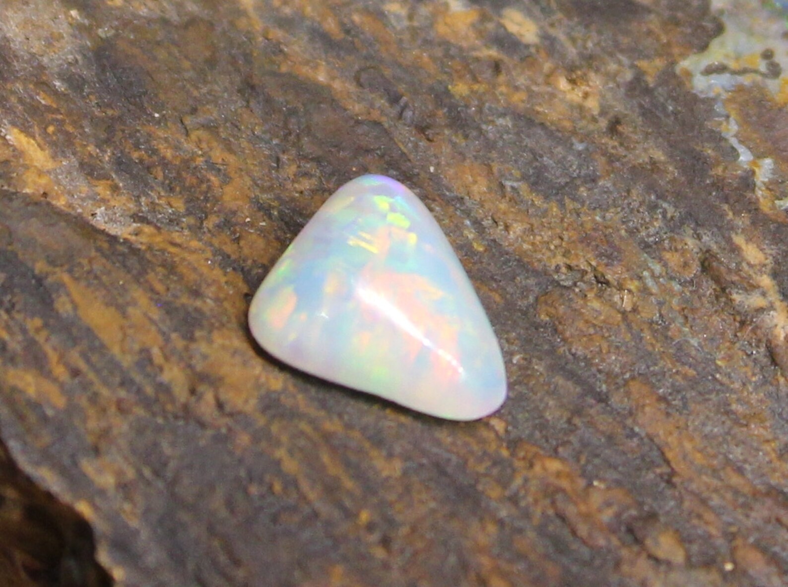 Triangular opal stone on a textured brown background