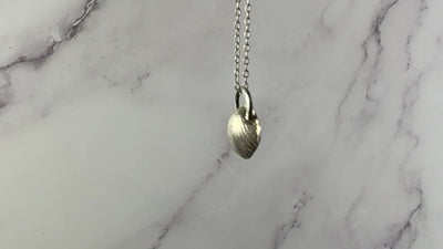 video of a sterling silver pendant in the shape of a seashell, swaying on a chain. Marble patterned background.