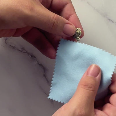 close up video of a sterling silver rose pendant necklace being polished with a small blue polishing cloth.