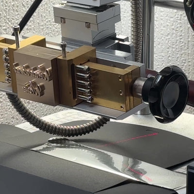 video of a hot foil stamping maching, in the machine is a brass block with a carving of text "wonderland white", the block is pressed into foil below, transferring the text onto a packaging box, which then as a foil deboss.