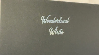 macro shot of a Lynne Lee packaging box, on the box is a silver foiled "wonderland white" tex, as the box moves back and forth, the foiled text catches the light.