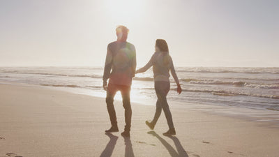 couple walking hand in hand along a beach. Bright sunlight makes the couple harder to see.