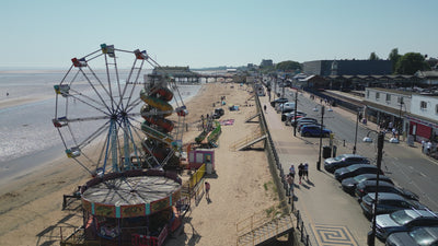 drone video moving along cleethorpes beach. The video shows a small funfair with ferris wheel and slide, the drone then moves towards the pier.