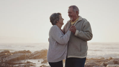 older couple dancing together in front of a beach.