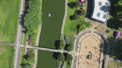 overhead video hovering over the Cleethorpes boating lake, going from south to north. Below are people in row boats, children playing in sand pits, people strolling.