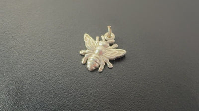 macro video of a sterling silver bee charm, the charming is rotating on a turntable.